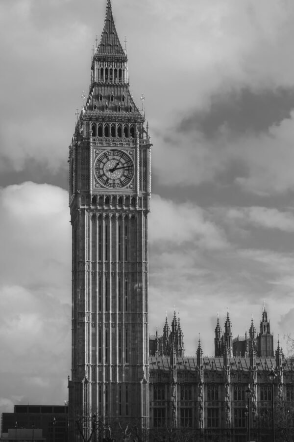 Black and white image of Big Ben and the Houses of Parliament in London against cloudy sky.