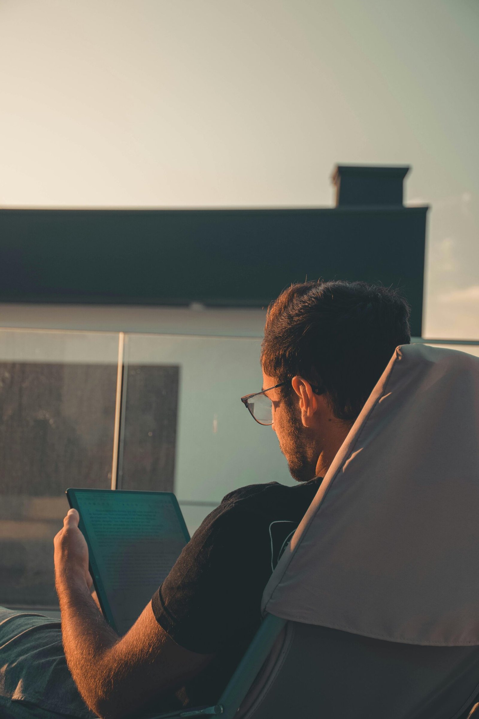 Adult man sitting outside reading on a digital tablet, enjoying a peaceful afternoon.