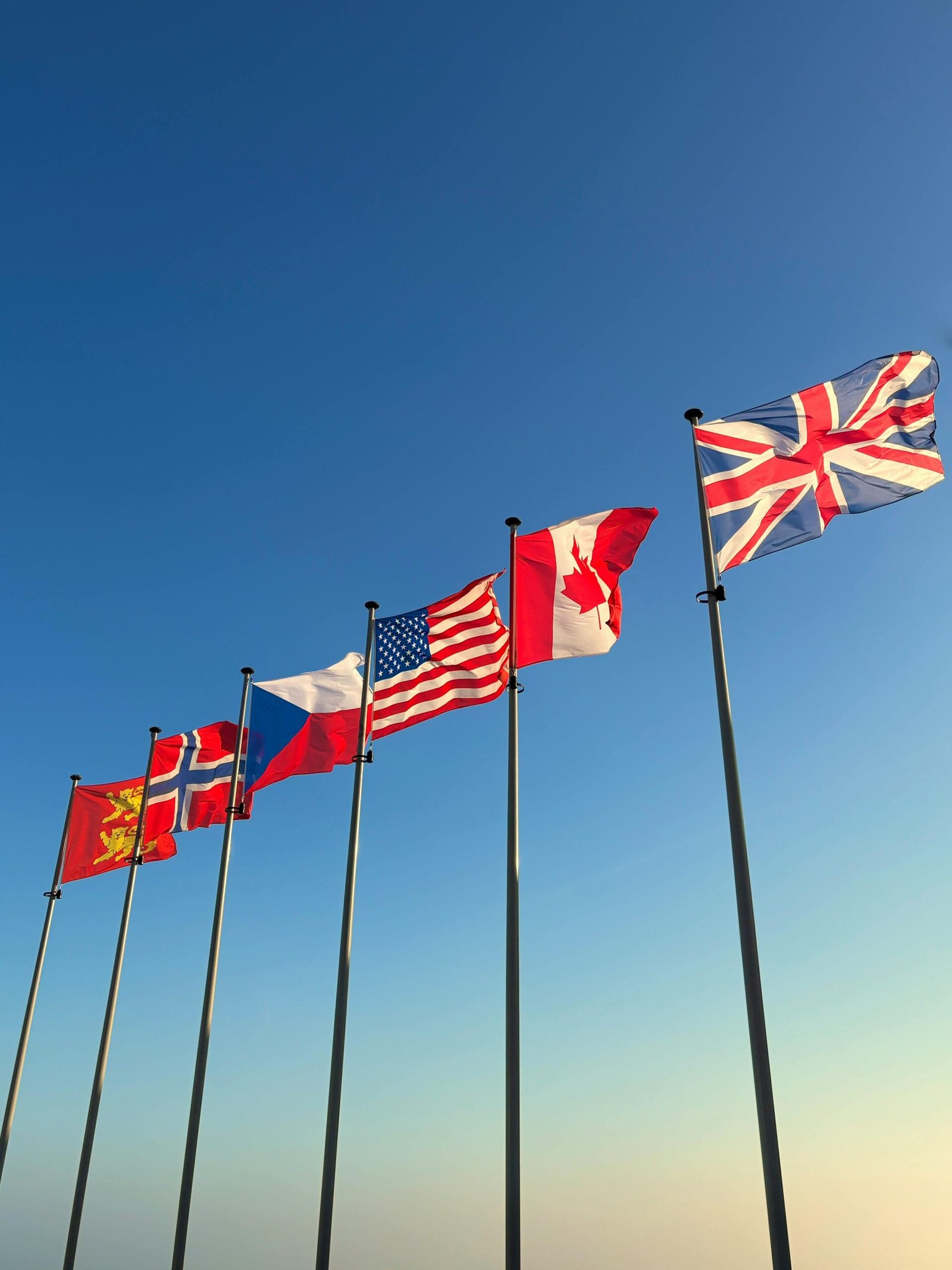 Flags of WWII allies waving at Arromanches-les-Bains, Normandie, France under a clear blue sky.