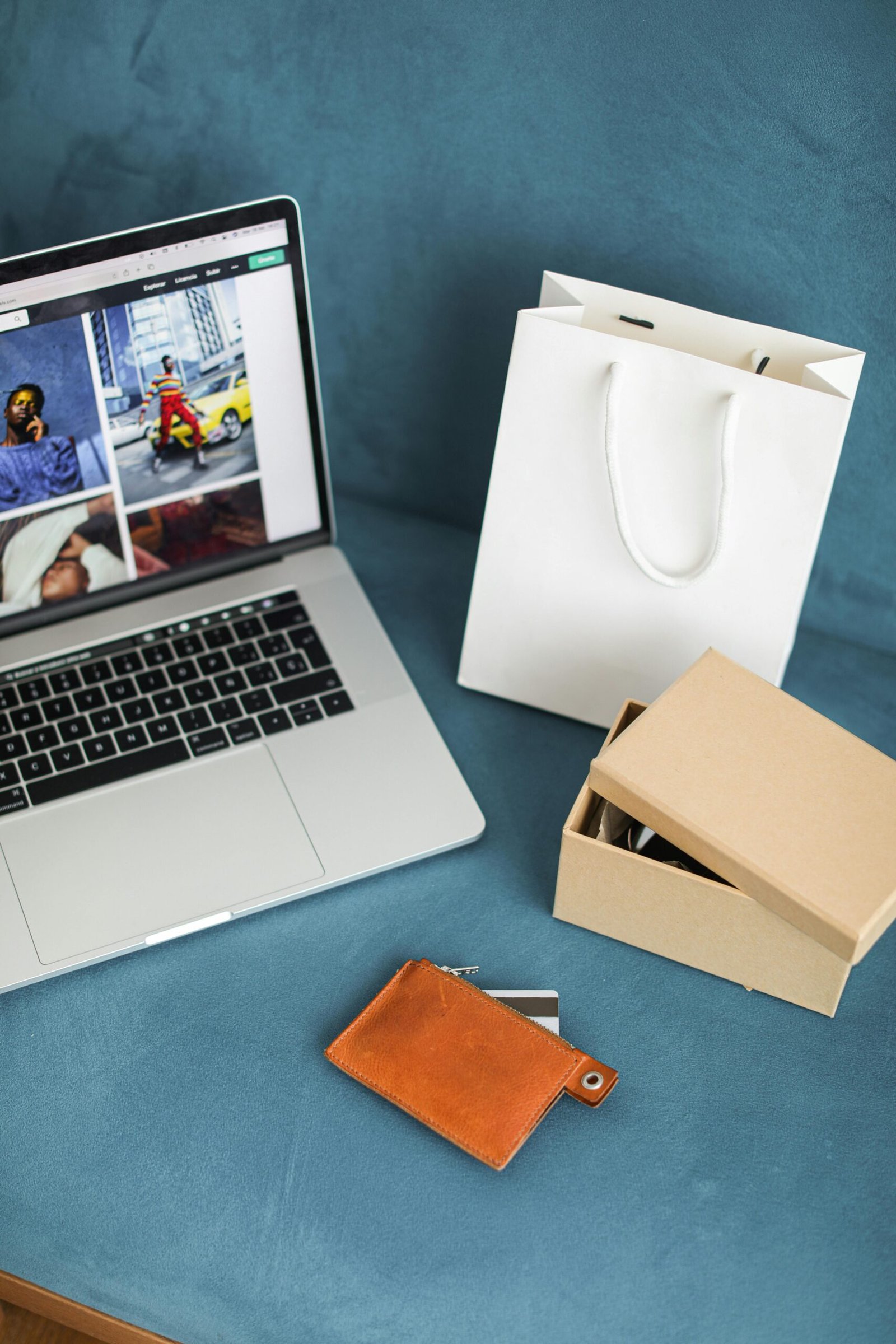A high-angle view of online shopping items including a laptop, gift bags, and wallet on a blue surface.
