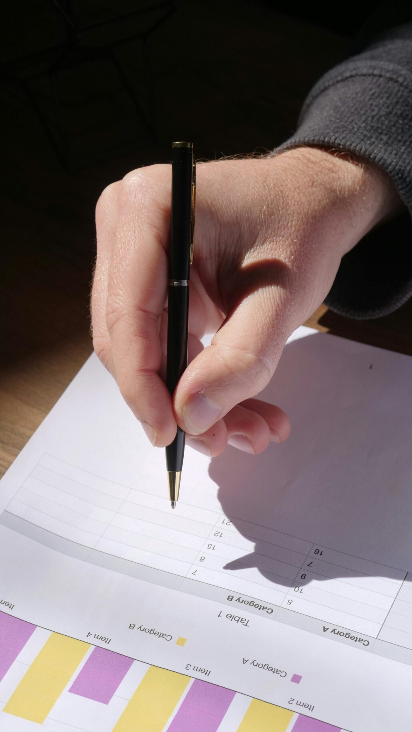Detailed image of a hand holding a black pen writing on a document in daylight.