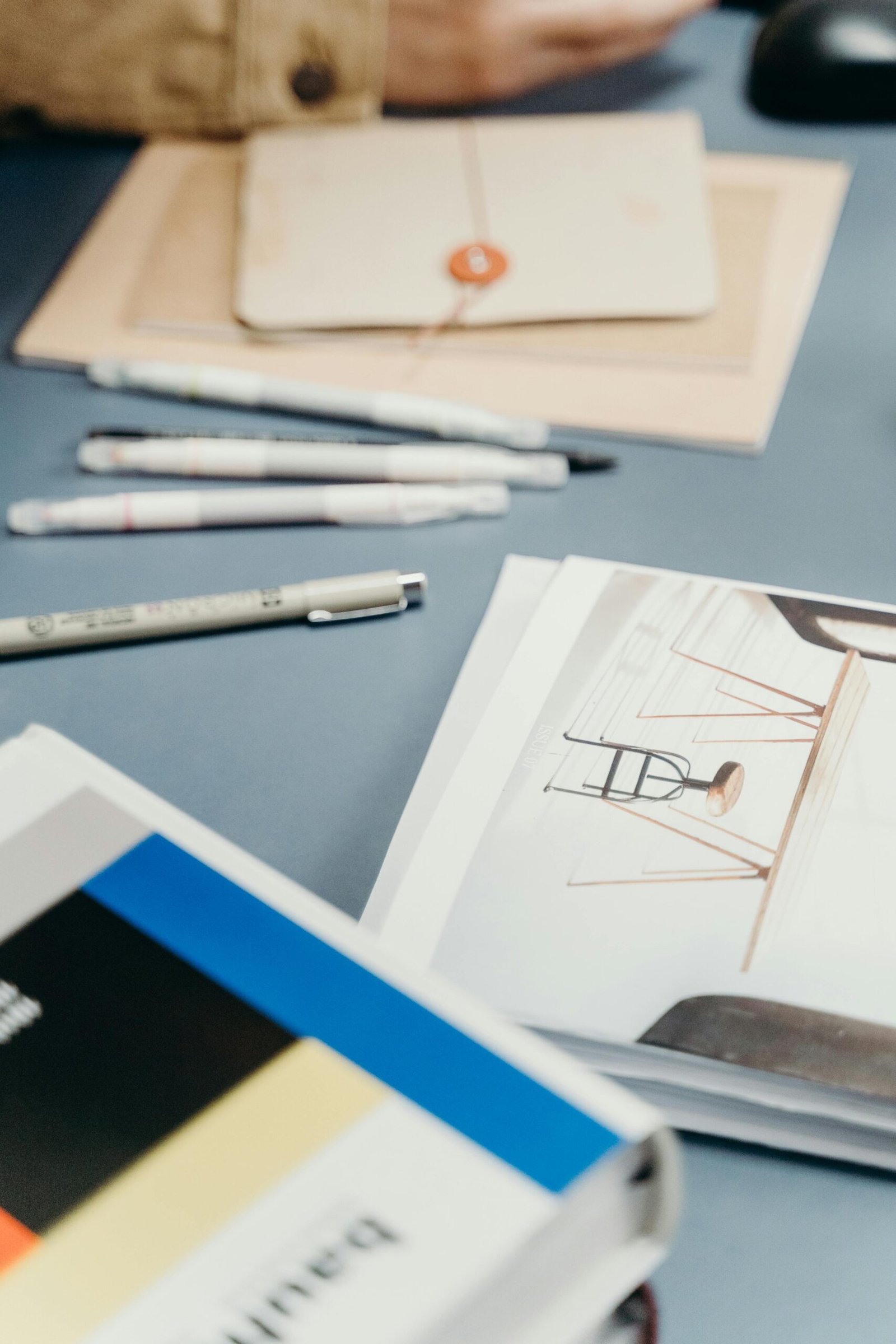A well-organized desk featuring notebooks, pens, and a design book for creative projects.