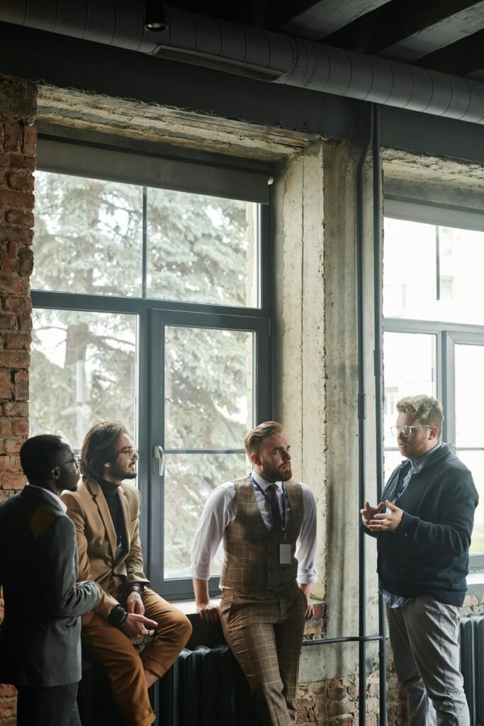 A group of diverse male professionals engaged in conversation by large windows.